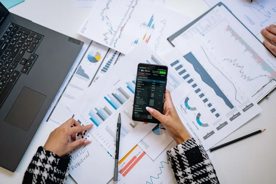 Hands typing on a laptop with cryptocurrency charts and smartphone display in view, focusing on digital finance.
